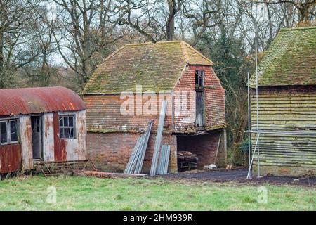 Un disuso e dilapidato, arrugginito, capannone di ferro ondulato e annessi agricoli in un campo a Vann, vicino Ockley, Surrey Foto Stock