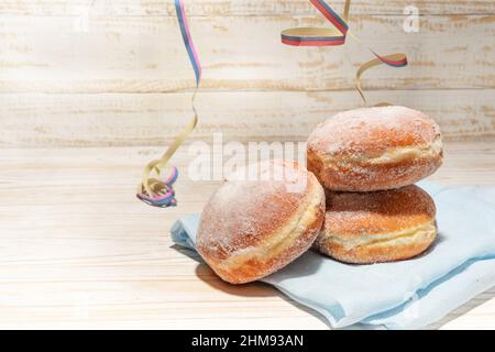 Ciambelle di Capodanno europeo e carnevale, chiamato Berliner o Krapfen su un tavolo di legno rustico chiaro con alcuni streamers partito, spazio copia, selezionato fo Foto Stock