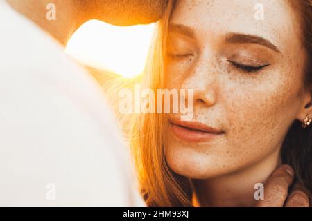 Primo piano ritratto di una frickled ragazza baciare dalla bocca del suo ragazzo. Vista ravvicinata di una coppia soleggiato. Viso di bellezza. Foto Stock