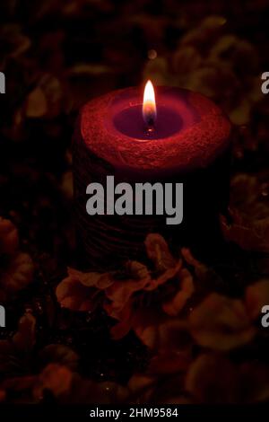 Una magica candela rossa brucia sullo sfondo nero con fiori. Foto Stock