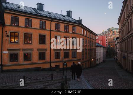 La gente cammina su una strada ciottolata svedese con edifici tradizionali a Sodermalm, a Natale al crepuscolo, a sud di Stoccolma, Svezia. Foto di alta qualità Foto Stock