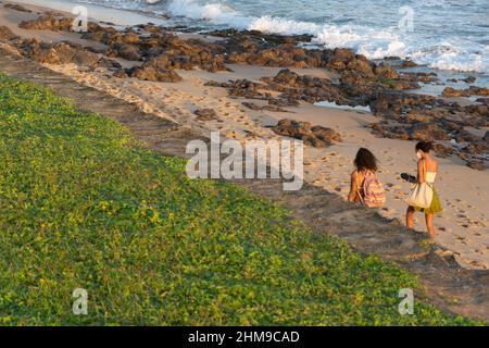 Due donne che camminano sulla sabbia della spiaggia di Paciencia nel quartiere Rio Vermelho a Salvador, Brasile. Foto Stock