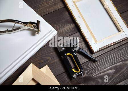 Tela che si allunga su barretta di legno. Foto stampata su tela (vista posteriore), martello, righello in acciaio e pistola a graffette su tavola di legno marrone Foto Stock