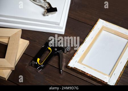 Tela che si allunga su barretta di legno. Foto stampata su tela (vista posteriore), martello, righello in acciaio e pistola a graffette su tavola di legno marrone Foto Stock