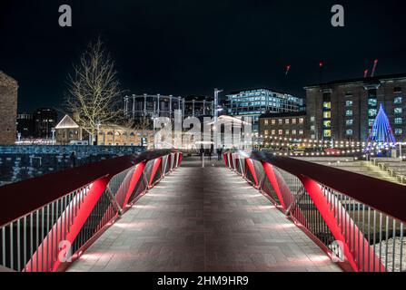 Ponte sul canale del Regent che conduce alla Piazza Granary, Coal Drops Yard, tutto illuminato di notte. Lo sviluppo dei Gasholders può essere visto in background. Foto Stock