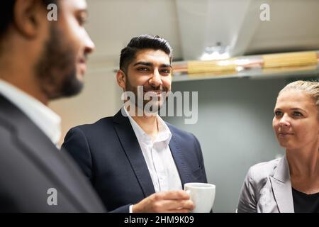 Tre giovani uomini d'affari come colleghi che hanno una piccola conversazione rilassata durante la pausa caffè in ufficio Foto Stock