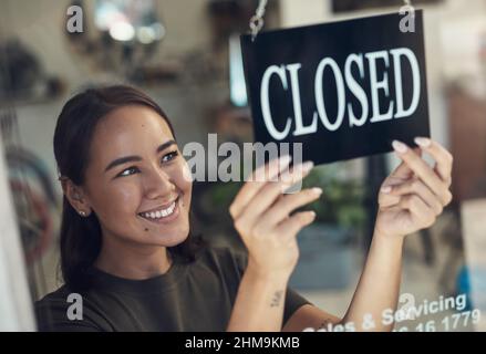 È stata una giornata così gratificante. Scatto di una giovane donna attraente in piedi e girare il segno sulla porta al suo negozio di biciclette. Foto Stock