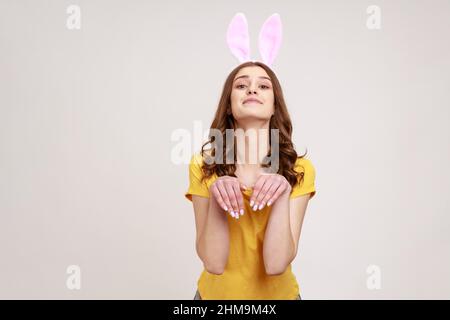 Ritratto di gioiosa bella donna di giovane età in giallo T-shirt che ha divertente infantile umorismo con le orecchie e le mani conigliate, divertente e ingannevole. Studio interno girato isolato su sfondo grigio. Foto Stock