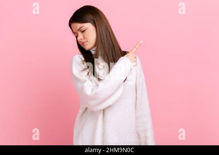 Ritratto di bruna giovane donna arrabbiata dito puntante, sneak maschio colpendo un'altra gente, indossando un pullover bianco casual stile. Studio interno girato isolato su sfondo rosa. Foto Stock