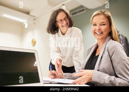 Due allegre donne d'affari stanno lavorando insieme con successo come squadra nella sala conferenze in ufficio Foto Stock