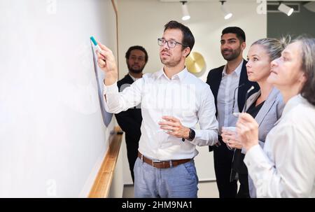 Giovane uomo d'affari e team di start-up aziendale che presenta la lavagna in ufficio Foto Stock