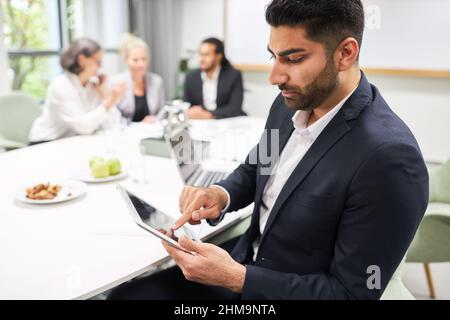 Uomo d'affari seduto al tavolo della conferenza durante la riunione e digitando sul touch screen del tablet Foto Stock