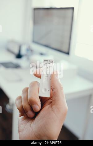 primo piano di un giovane in ufficio che ha in mano un covid-19 antigene diagnostico dispositivo di prova con un risultato positivo Foto Stock