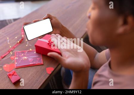 Il giovane africano americano che soffia bacio sullo smartphone con spazio vuoto durante le videochiamate Foto Stock
