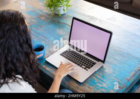 Vista ad alto angolo della giovane donna biraciale utilizzando un computer portatile con schermo vuoto mentre si beve in un bar Foto Stock