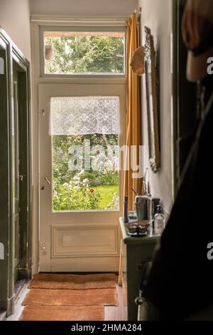 Interno di corridoio con porta di legno e tappeti in cottage vecchio stile che conduce al giardino Foto Stock