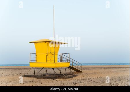 Torre di bagnino giallo luminoso situata su una spiaggia sabbiosa vuota vicino al mare contro il cielo blu nuvoloso Foto Stock