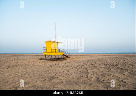 Torre di bagnino giallo luminoso situata su una spiaggia sabbiosa vuota vicino al mare contro il cielo blu nuvoloso Foto Stock