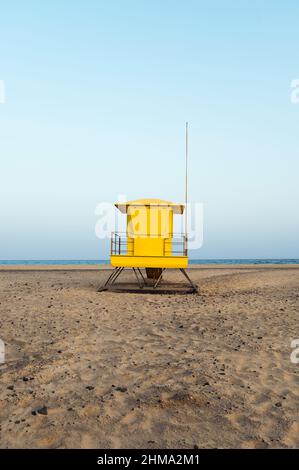 Torre di bagnino giallo luminoso situata su una spiaggia sabbiosa vuota vicino al mare contro il cielo blu nuvoloso Foto Stock