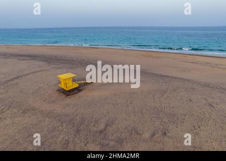 Spettacolare vista aerea della torre del bagnino giallo luminoso situata sulla spiaggia sabbiosa di fronte al mare blu sotto il cielo solato Foto Stock