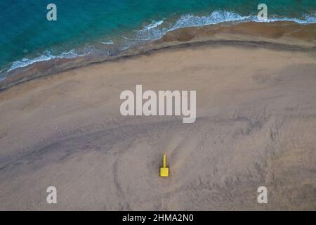 Spettacolare vista aerea dall'alto della torre del bagnino giallo luminoso situata sulla spiaggia sabbiosa di fronte al mare blu sotto il cielo solato Foto Stock