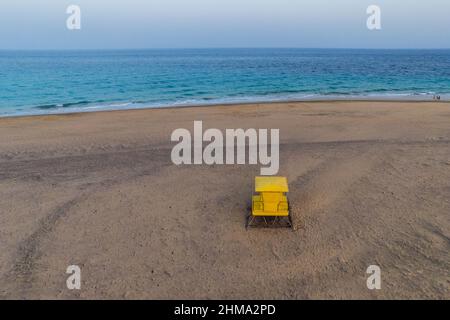 Spettacolare vista aerea della torre del bagnino giallo luminoso situata sulla spiaggia sabbiosa di fronte al mare blu sotto il cielo solato Foto Stock