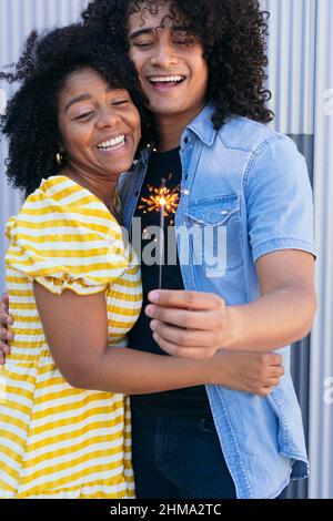 Gioiosa coppia ispanica con ricci afro abbracciando teneramente e scintillio ardente per un'occasione speciale di festa Foto Stock