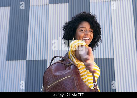 Vista posteriore della femmina ispanica con capelli ricci sorridendo piacevolmente mentre si raggiunge la mano per il supporto e guardando la macchina fotografica Foto Stock