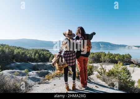 Vista posteriore completa del corpo di una coppia amorevole che si ergono su formazioni rocciose e si abbracciano mentre si trascorre una giornata di sole sulla riva del lago Foto Stock