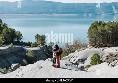 Vista laterale del corpo di una coppia amorevole che si alza su formazioni rocciose e si abbraccia mentre si passa la giornata di sole sulla riva del lago Foto Stock