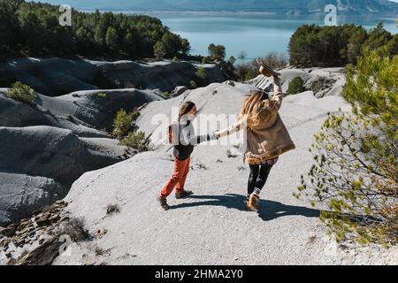 Vista posteriore del corpo della coppia in piedi su terra di pietra e ammirando il lago circondato da colline sotto il cielo blu Foto Stock