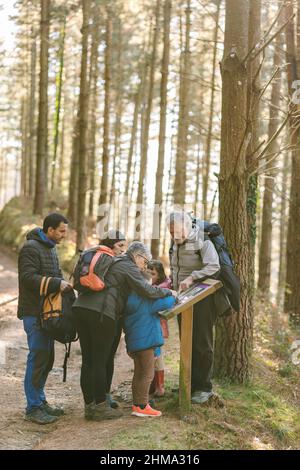 Famiglia di escursionisti con bambini che leggono informazioni su tavola di legno mentre in piedi sul sentiero nei boschi in autunno durante il trekking Foto Stock