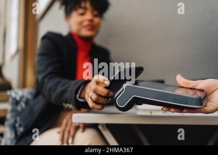Crop African American femmina cliente mettere il cellulare sul terminale in mano alla cameriera e pagare per l'ordine in caffetteria Foto Stock