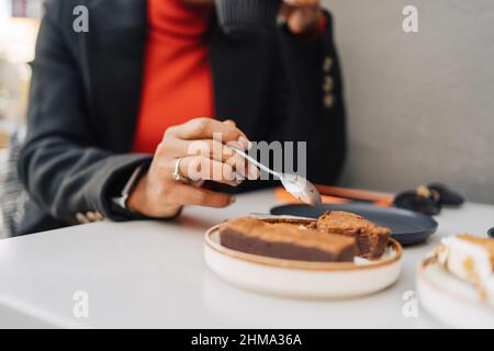 Coltivare irriconoscibile afroamericana femmina mangiare dolce torta con cucchiaio in caffetteria Foto Stock