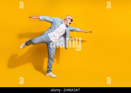 Vista a tutta lunghezza del corpo di attraente allegro motivato uomo grigio-capelli che ha divertimento volare isolato su sfondo giallo chiaro Foto Stock