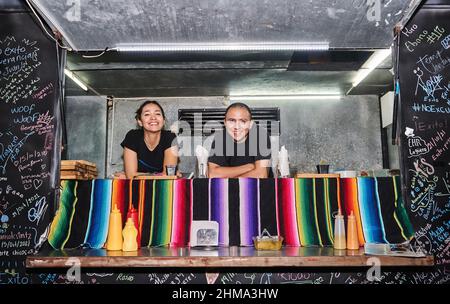 Dipendenti etnici maschi e femmine in piedi al banco del camion alimentare e guardando la macchina fotografica con sorriso Foto Stock