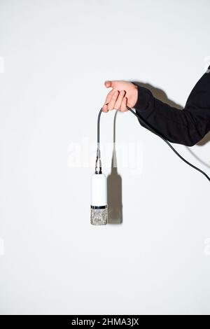Mano di raccolto anonimo cantante in nero con microfono professionale su filo in piedi in studio luce su sfondo bianco Foto Stock