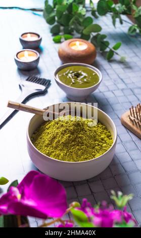 Da sopra composizione con ciotola di henné in polvere morto vicino spazzola pettine di legno e candele brucianti per la cura naturale dei capelli Foto Stock