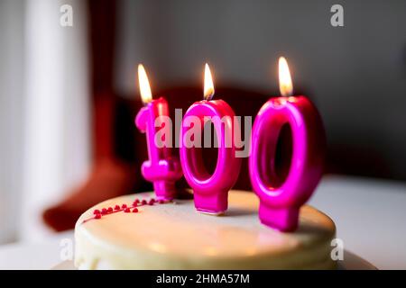 Candele brucianti con numero 100 su dolce torta di compleanno preparato per festeggiare e messo sul tavolo Foto Stock