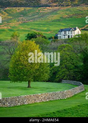 Paesaggio Wharfedale campagna (grande casa, pendii della valle, curvare muro di pietra a secco, pascoli e campi di terra verde alta) - Yorkshire Dales, Inghilterra Regno Unito. Foto Stock