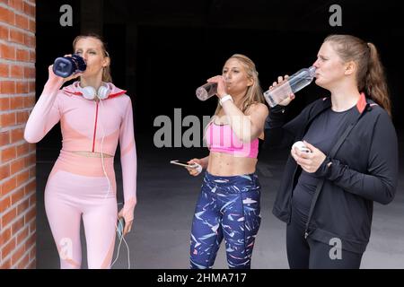 Sport belle donne giovani di diversi tipi di corpo bere acqua dalla bottiglia dopo aver allenato fuori da una palestra, palestra, fitness, concetto sportivo . Foto di alta qualità Foto Stock