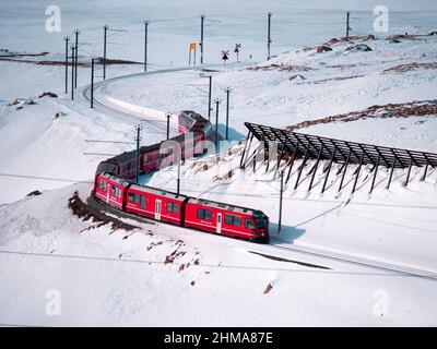 Berninapass, Svizzera - 19 gennaio 2022: Treno panoramico turistico rosso Bernina Express che corre tra Chur e Tirano in Italia e attraversa la neve cov Foto Stock