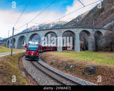 Brusio, Svizzera - 3 febbraio 2022: Ferrovia Retica nei paesaggi di Albula e Bernina. Patrimonio dell'umanità dell'UNESCO - treno espresso Bernina all'elicoidale Foto Stock