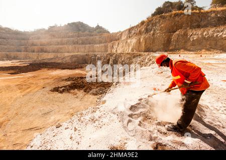 Un minatore identificato che indossa una maschera facciale, un casco e un'attrezzatura di protezione che lavora con uno strumento di estrazione in ambienti polverosi e caldi in una cava mineraria. Foto Stock