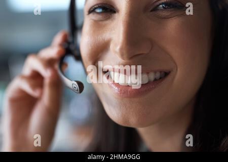 Più grande è il sorriso, migliore è il servizio. Ritratto di una giovane donna che utilizza una cuffia in un ufficio moderno. Foto Stock