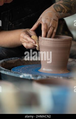 Mani che formano un pezzo di argilla in una pentola su una ruota di ceramica Foto Stock