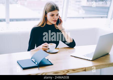 Assistente amministrativo che beve una bevanda calda e parla al telefono cellulare Foto Stock