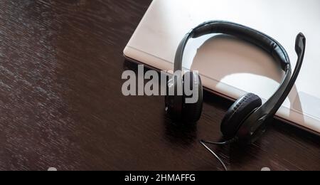 Auricolare su un computer portatile, tavolo in legno, vista dall'alto, spazio copia, call center, ufficio domestico, assistenza clienti, help desk Foto Stock
