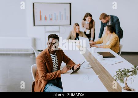 Bel giovane uomo d'affari afroamericano che lavora con un tablet digitale davanti ai suoi colleghi nella sala riunioni Foto Stock