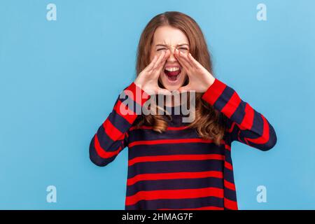 Ritratto di donna arrabbiata apre la bocca ampiamente, urla in panico, scopre notizie horror, essere in una situazione stressante, indossare a righe casual stile maglione Indoor studio girato isolato su sfondo blu. Foto Stock